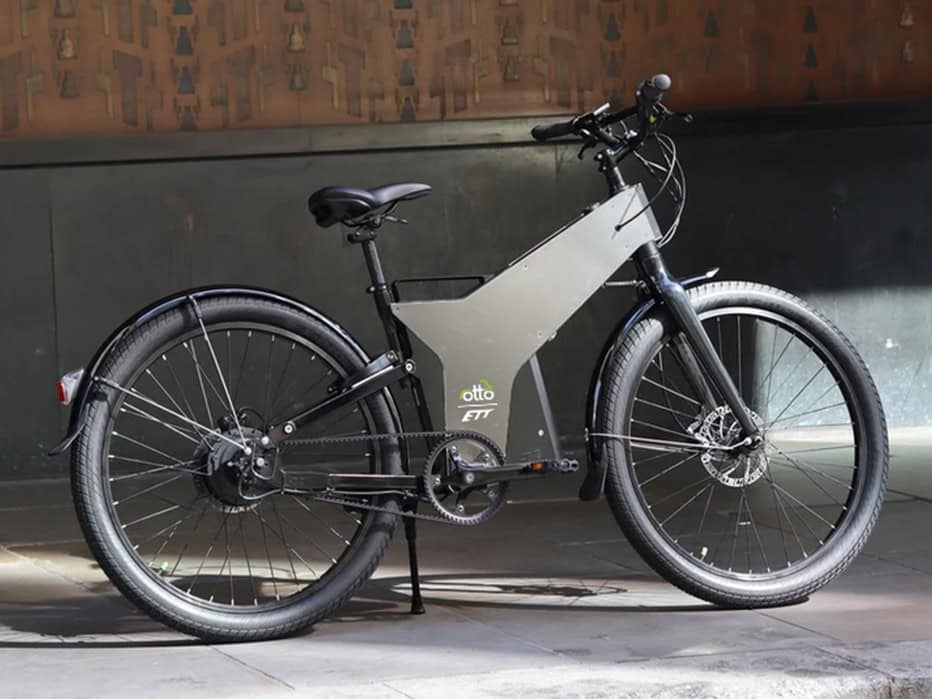 A Sleek, Matte Gray E-bike With Thick Tires And A Curved Frame Stands Parked Indoors On A Tiled Floor, Ready For Its Next Uber Eats Delivery. The Addition Of A Practical Rear Fender Ensures It Handles London's Unpredictable Weather With Ease.